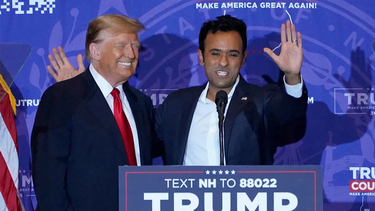 former president 45 donald trump standing on stage with presidential candidate and vice president candidate vivek ramaswamy in front of a blue background with a TUMP speaker station in front of them both. vivek is on the right holding his left hand up waving at the crowd as he smile and waves at the crowd in new hampshire after announcing his endorsement of president donald trump in the 2024 united states presidential election.